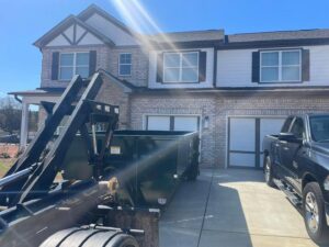 An empty green dumpster being delivered or picked up from a residential driveway by Beetles Dumpsters Rental & Junk Removal in Huntsville, AL.