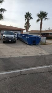 An empty blue Tidy up time dumpster placed in a residential driveway for upcoming junk removal in El Paso, TX.