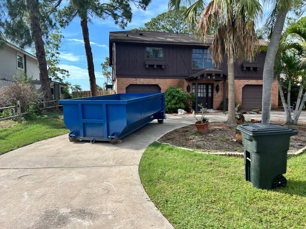 An empty blue dumpster placed on a residential driveway for junk removal by R&Y Dumpster Kings in Tampa, FL.