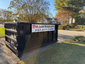 An empty black dumpster from The Junk Ninjas placed in a residential setting, ready for junk removal in Hampton Roads, VA.