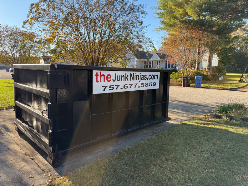 An empty black dumpster from The Junk Ninjas placed in a residential setting, ready for junk removal in Hampton Roads, VA.