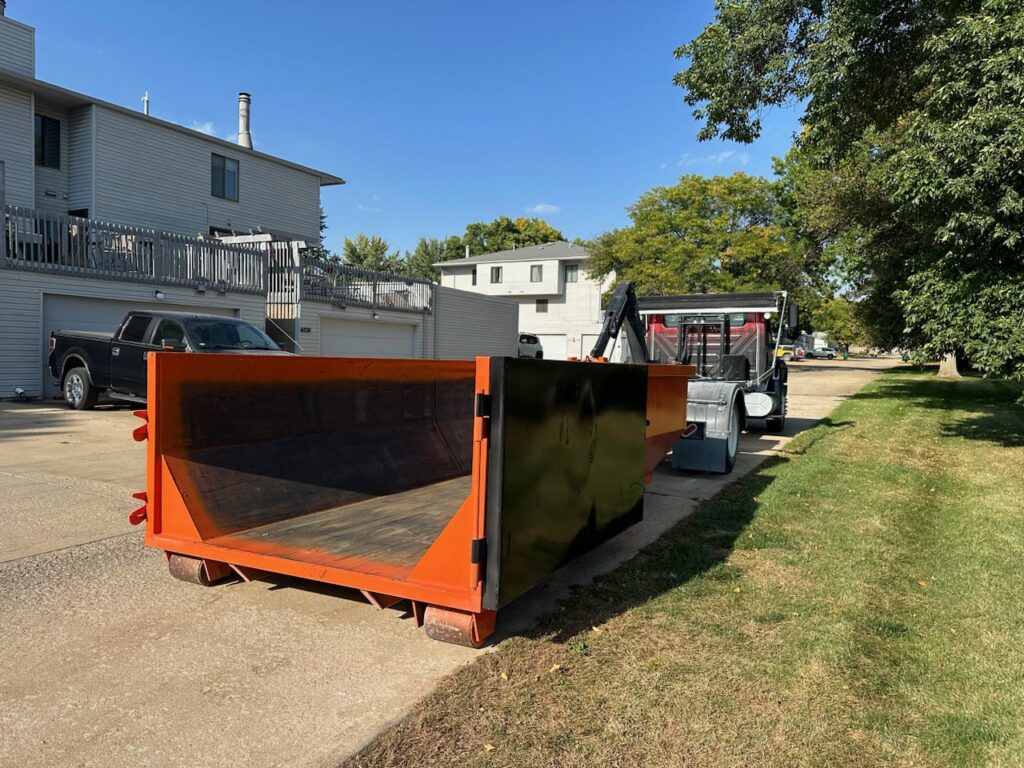 An empty orange dumpster placed on a residential street by All Seasons Junk Removal & Dumpster Services in Center Point, IA.