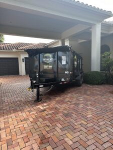 An empty Driveway Safe Dumpster Rental trailer parked under a covered driveway, ready for a junk removal job in Fort Lauderdale, FL.