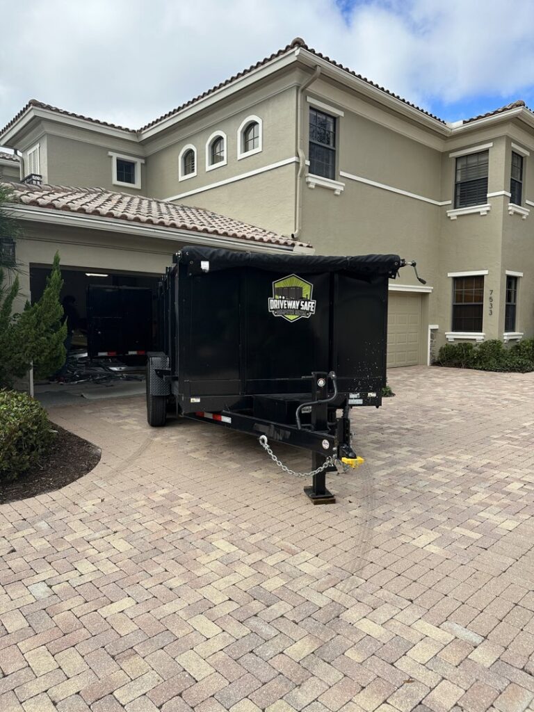 An empty Driveway Safe Dumpster Rental trailer parked on a paved driveway in front of a large house in Fort Lauderdale, FL, ready for a cleanup.