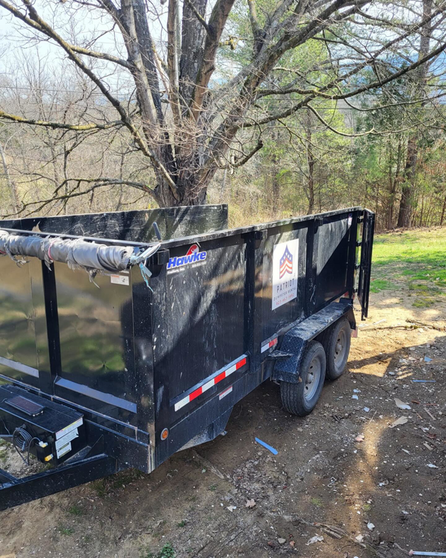 An empty black dump trailer with the Patriot Dumpster Rental logo parked outdoors in Chattanooga, TN.