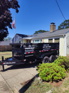 An empty dumpster trailer from Dumpsters RI.com - Dumpster Rentals RI parked in a residential driveway on a sunny day in Rhode Island.