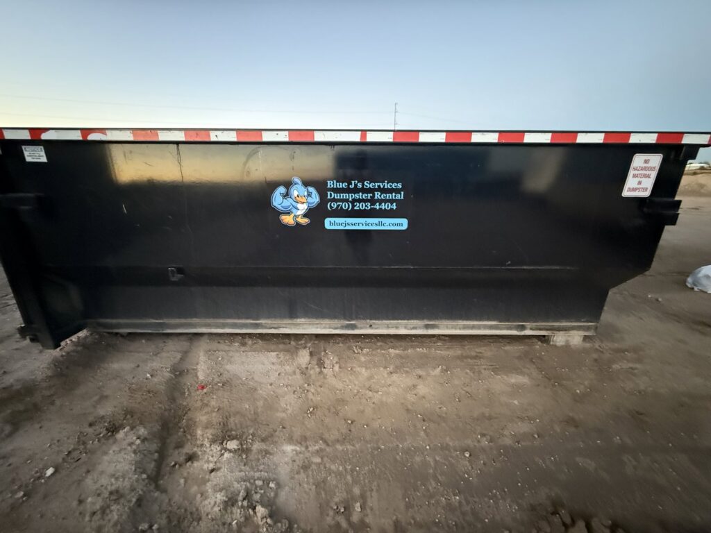 An empty black dumpster with the Blue J's Services Dumpster Rental logo and contact information visible in Greeley, CO.