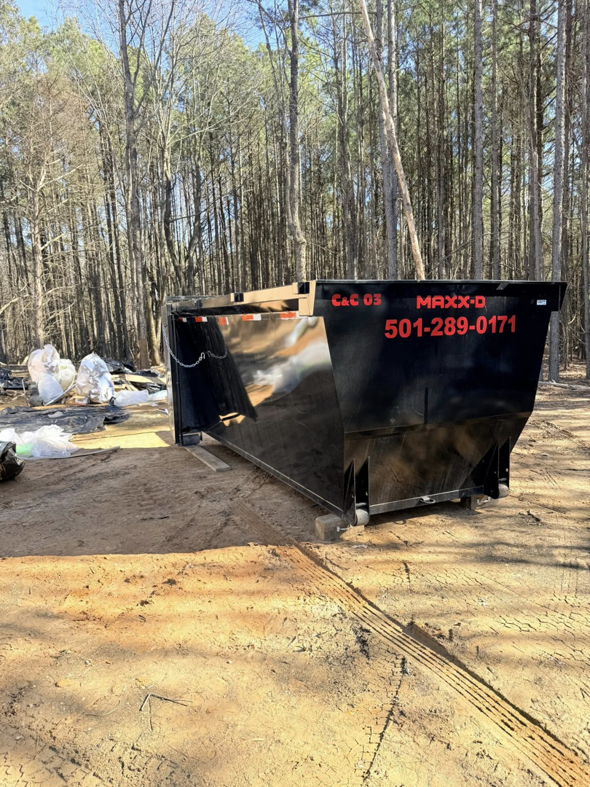 An empty dumpster from C&C Dumpster Rentals LLC placed in a wooded area for junk removal in Conway, AR.