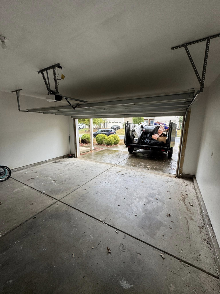 An empty garage with a Junkjet truck and trailer full of removed items visible outside in Charlotte, NC.