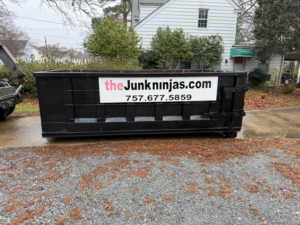 An empty black dumpster from The Junk Ninjas being delivered or picked up on a gravel driveway in Hampton Roads, VA.