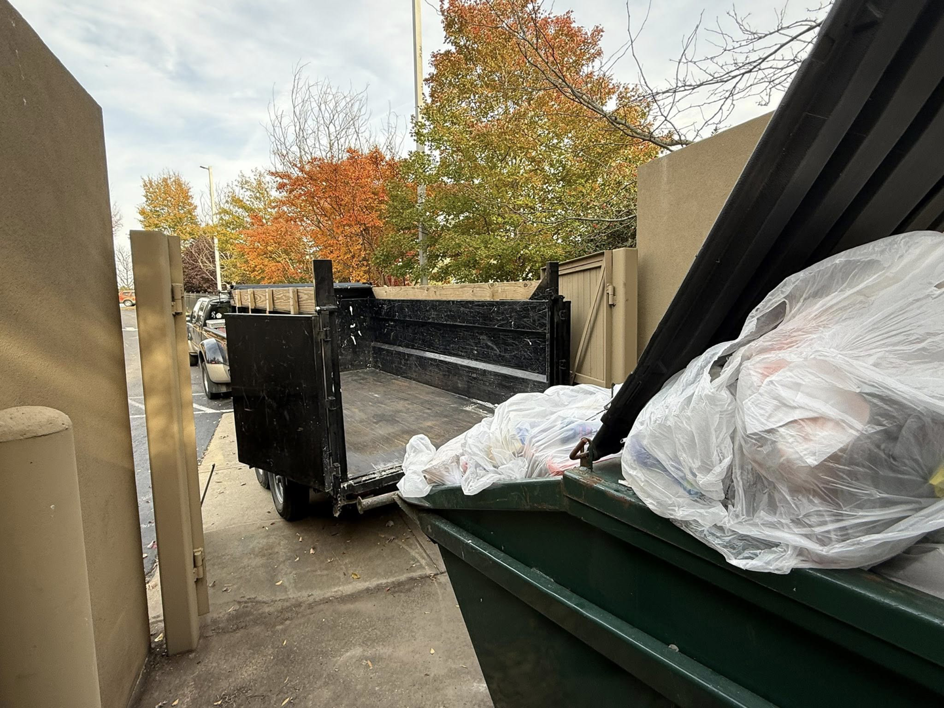 An empty junk removal trailer backed up to a commercial dumpster, ready for loading by Freedom Hauling in California, MD.