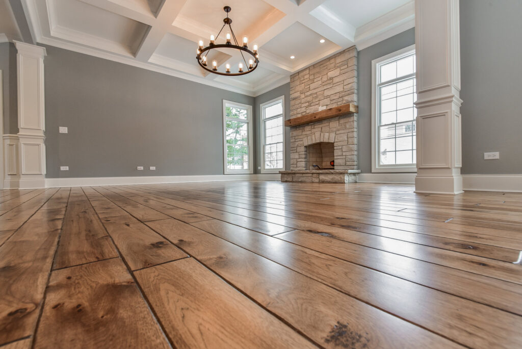 An empty living room with hardwood floors, a stone fireplace, and coffered ceiling, built by Autumn Homes in Naperville, IL.