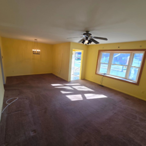An empty living room with yellow walls and brown carpet, ready for handyman services like painting or flooring from 1st State's Finest LLC in Middletown, DE.