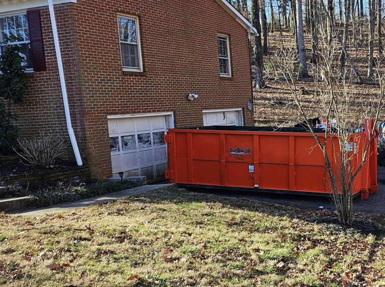 An empty orange roll-off dumpster ready for junk removal rental in a residential driveway from Haul Rollers LLC in Roanoke, VA.