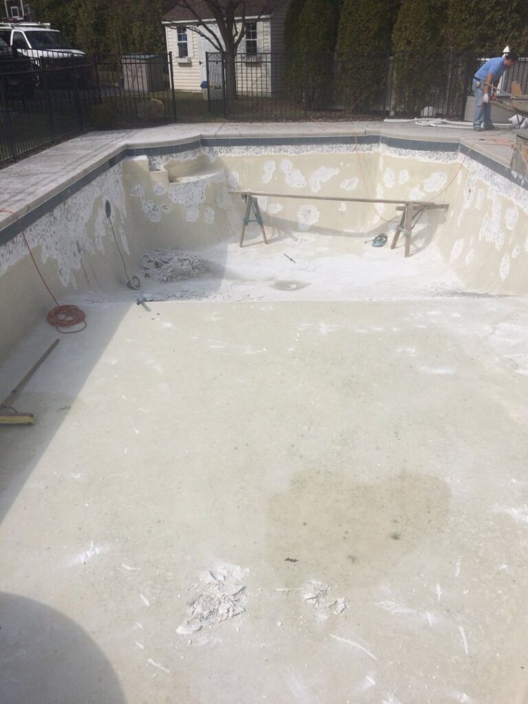 An empty swimming pool being prepared for resurfacing or repair, with a worker in the background, by B-rod Pool Service LLC in Norwalk, CT.