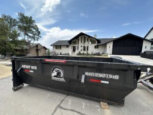 An empty RAAAM Dumpster Rentals dumpster placed on a residential street in front of a large home in Salt Lake City, UT.