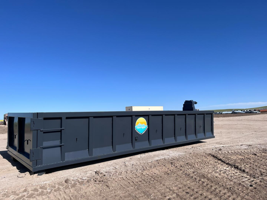 A large, empty roll-off dumpster from First Light Services Llc, ready for junk removal on a dirt lot in Casper, WY.