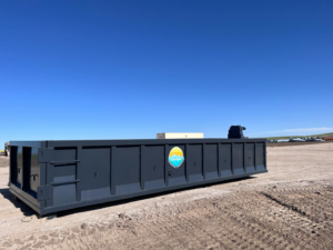 A large, empty roll-off dumpster from First Light Services Llc, ready for junk removal on a dirt lot in Casper, WY.