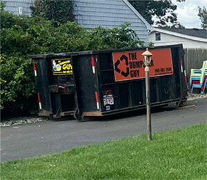 An empty roll-off dumpster from The Dumpster Guy, placed on a residential driveway for junk removal in Webster, MA.