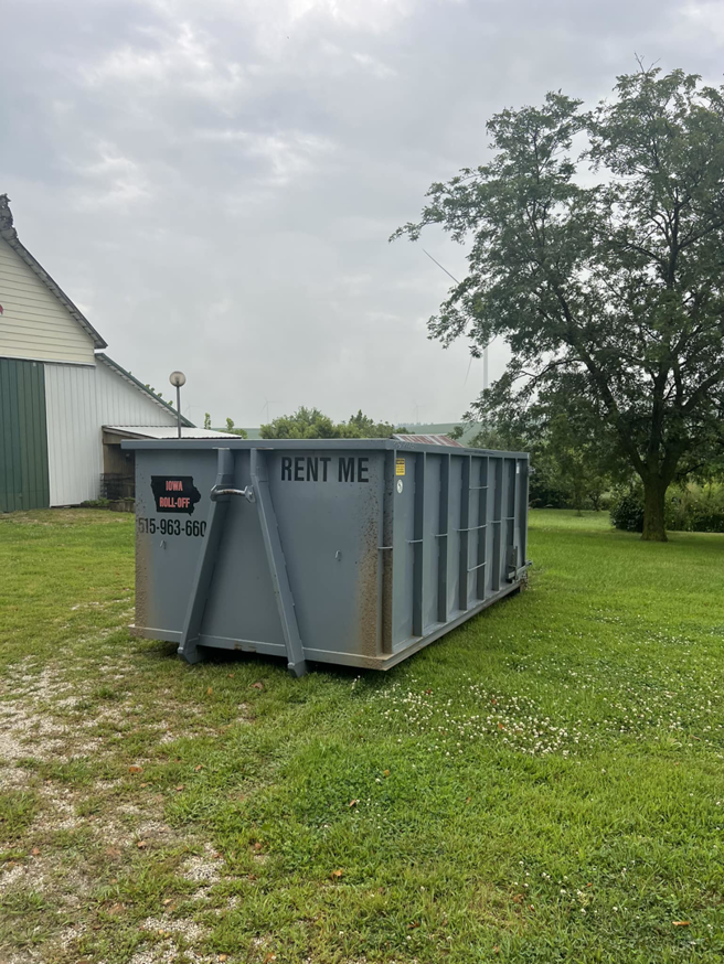 An empty grey roll-off dumpster placed in a grassy area, available for rent from Iowa Roll Off in Ankeny, IA.