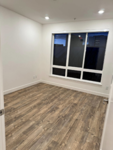 A bright empty room with new wood-look flooring, white walls, and a large window completed by Alitos Handyman in San Jose, CA.
