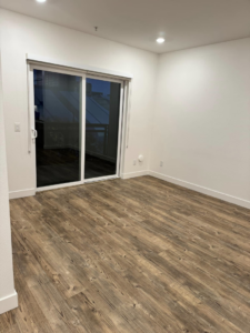 An empty room featuring new wood-look flooring, white walls, and a sliding glass door by Alitos Handyman in San Jose, CA.