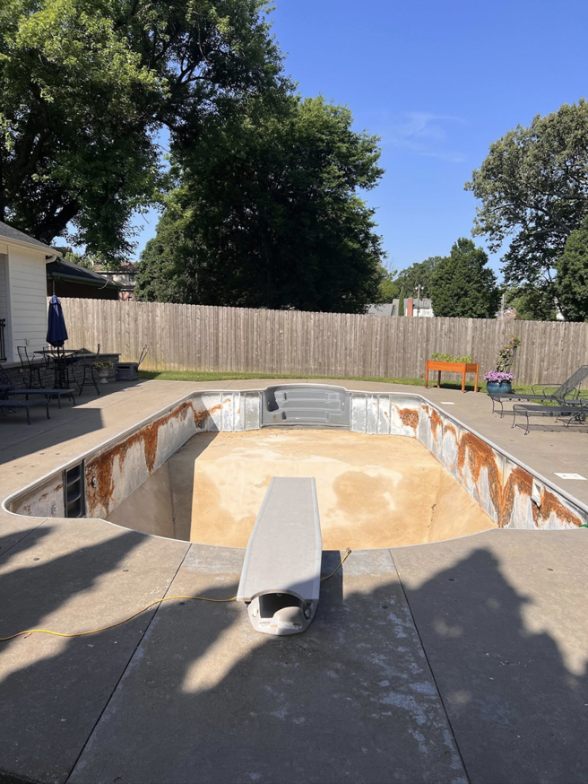 An empty swimming pool with a diving board and rust stains, awaiting cleaning by Premier Power Washing in East Islip, NY