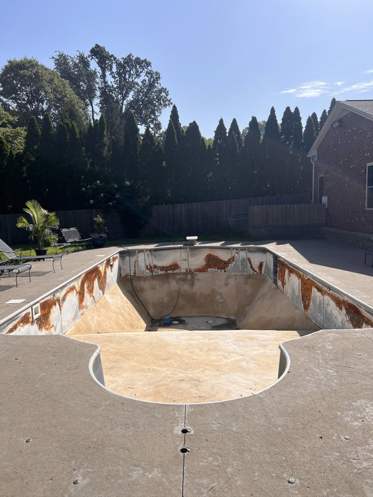 An empty swimming pool with significant rust stains on the walls, before cleaning by Premier Power Washing in East Islip, NY
