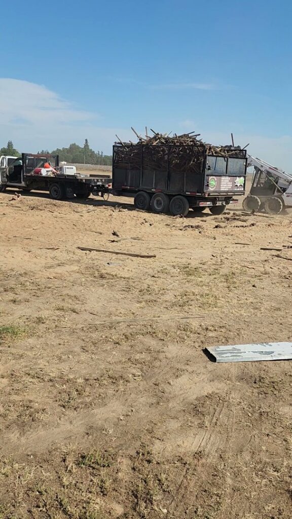 Workers from Haul-R-Us Junk Removal LLC clearing a large pile of junk, including tarps and shopping carts, in Fresno, CA.