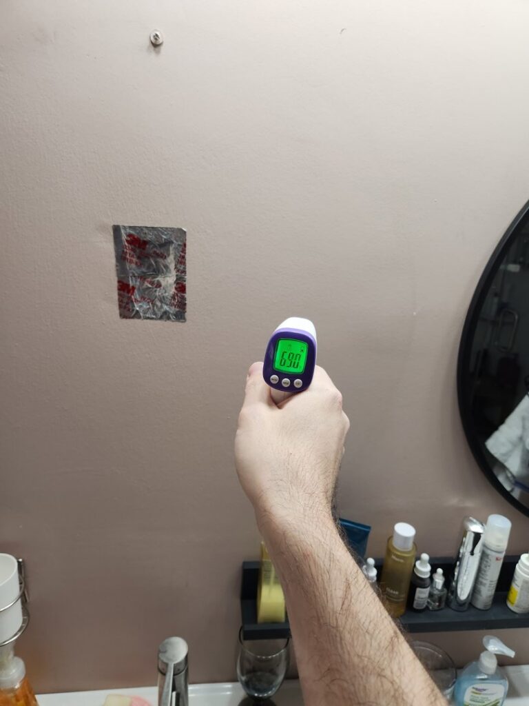 Handyman performing an energy audit with an infrared thermometer on a wall for Miami Valley Insulation Co LLC in Dayton, OH.