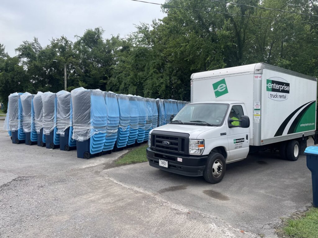An Enterprise rental truck parked next to a large stack of new blue trash bins from One Waste Solutions in Murfreesboro, TN.
