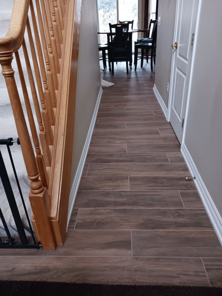 An entryway and hallway with new wood-look tile flooring and a wooden staircase by Home Improvement Design Center in Ann Arbor, MI.