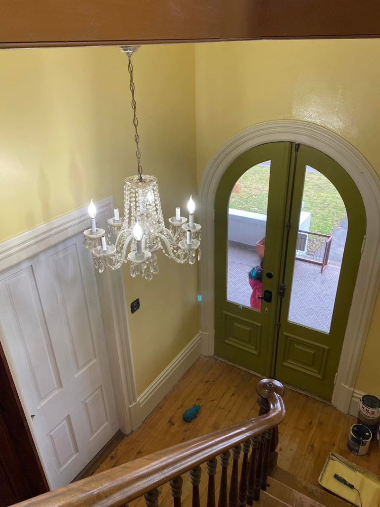An entryway with freshly painted yellow walls, a chandelier, and green arched doors, with paint cans on the floor indicating a painting job by Tucker Paint & Construction in Fulton, Canton, OH.