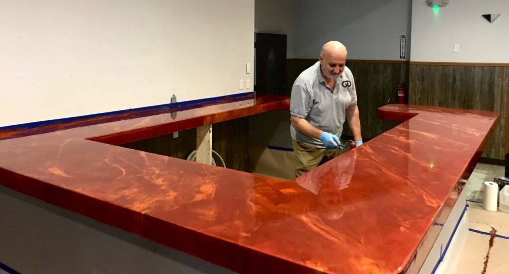 A handyman applying an epoxy finish to a custom red bar countertop for Coastal Surface Design in Virginia Beach, VA.