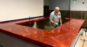 A handyman applying an epoxy finish to a custom red bar countertop for Coastal Surface Design in Virginia Beach, VA.