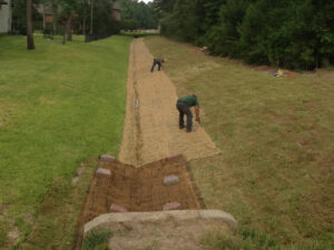 Workers installing erosion control matting in a drainage ditch by Daniel Dean Land Clearing & Dirt Work in Houston, TX.