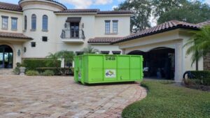A green dumpster placed in a large estate driveway for junk removal by Bin There Dump That Dumpster Rental Orlando, FL.