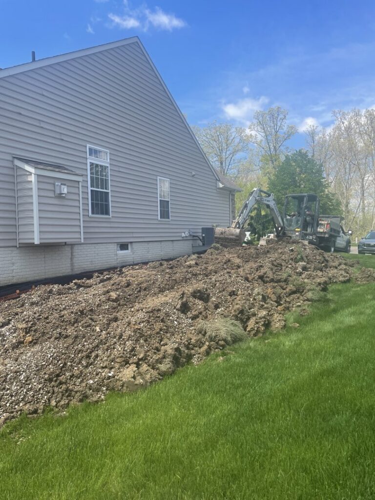 Large pile of excavated dirt next to a house foundation, indicating ongoing basement work by Pioneer Basement Solutions in Canton, OH.