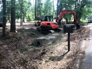 Excavator and skid steer performing drainage installation near a mailbox by Daniel Dean Land Clearing & Dirt Work in Houston, TX.
