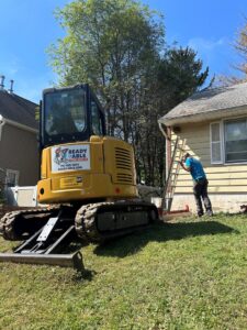 An excavator and a worker on a ladder performing exterior renovation work on a house by Ready & Able in Etters, PA.