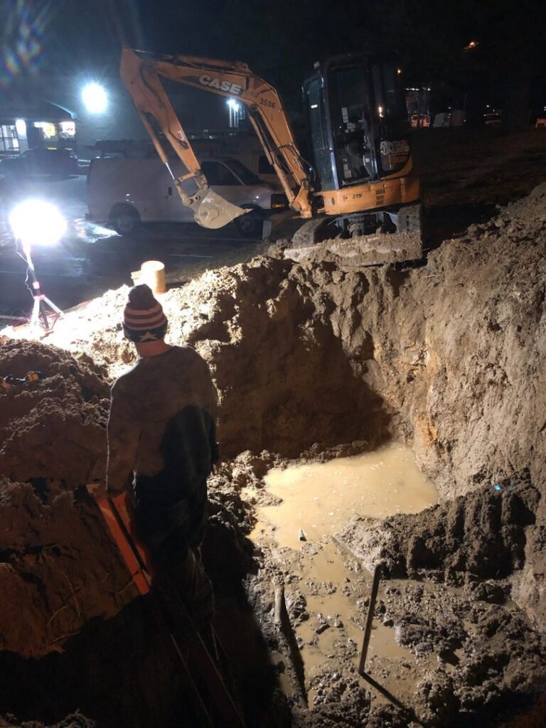 A worker overseeing a large excavation for plumbing repair at night by JF Plumbing & Heating in Rockville, MD.