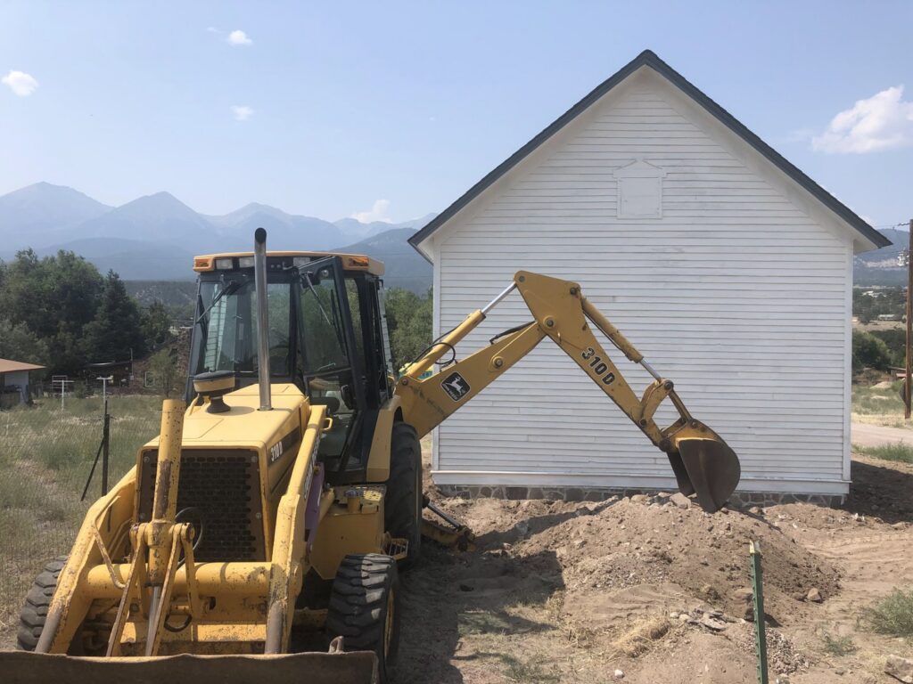 Excavation work with a backhoe next to a building, preparing the site by Deep Roots Craftsmen in Fort Collins, CO.