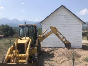 Excavation work with a backhoe next to a building, preparing the site by Deep Roots Craftsmen in Fort Collins, CO.