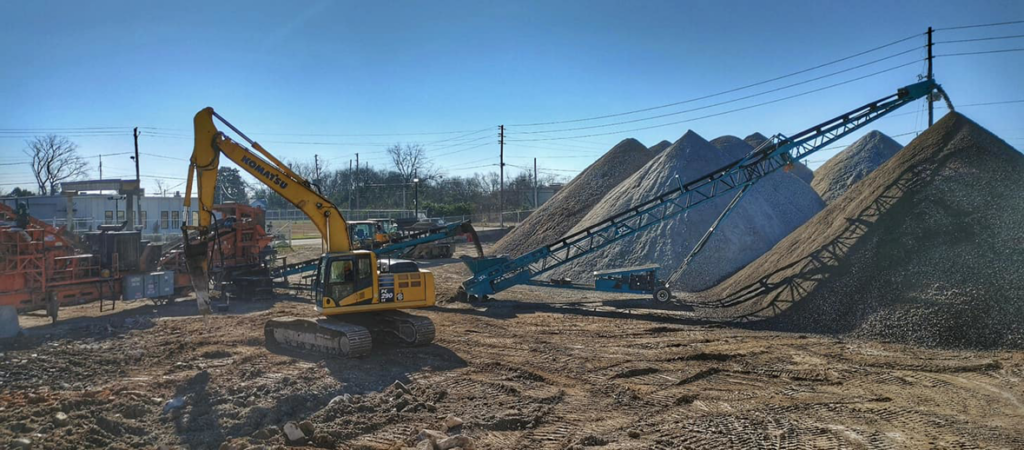 An excavator and conveyor belt with large piles of aggregate at Eco Recycling Group in Macon, GA