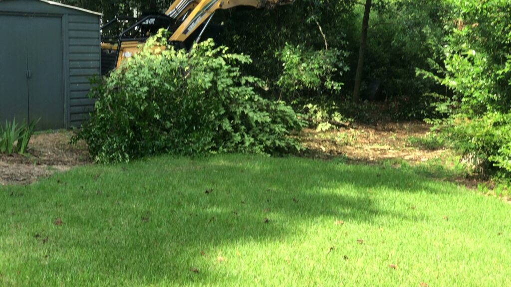 An excavator clearing branches and debris near a shed, demonstrating cleanup services by Jon's Tree Service in Pelham, AL.