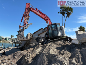 An excavator from White Star Services LLC clearing concrete debris next to a waterway in Corpus Christi, TX.
