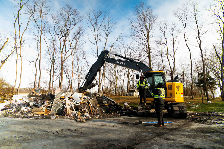 An excavator and crew from Limitless Hauling & Junk Removal clearing a large pile of demolition debris in Troy, OH.