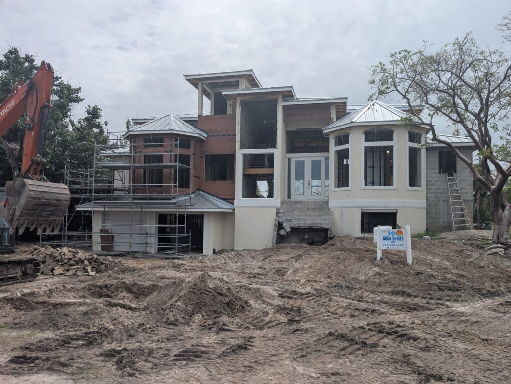 An excavator on a custom home construction site with scaffolding and a 'Rock Homes' sign by Rock's Custom Homes in St. Petersburg, FL.