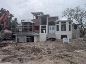 An excavator on a custom home construction site with scaffolding and a 'Rock Homes' sign by Rock's Custom Homes in St. Petersburg, FL.