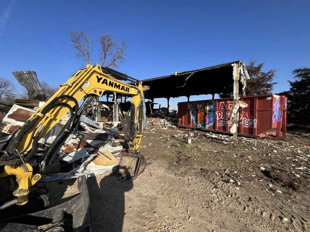 An excavator next to a demolished structure and a red roll-off dumpster from AT Disposal in Dewitt, IA.